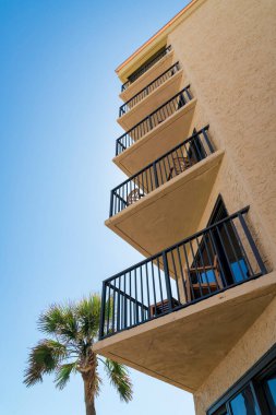 Destin, Florida 'da üçgen köşeli balkonlar alçak açılı. Dış tarafı sarı desenli duvar ve balkonlarda çelik korkuluklar ve solda bir palmiye ağacı manzaralı..