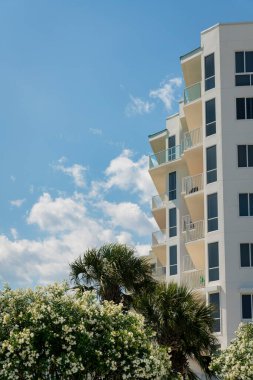 Destin, Florida 'da balkonları ve renkli camları olan bir binanın manzarası. Gökyüzüne karşı çok katlı binanın altında ağaçlar var..