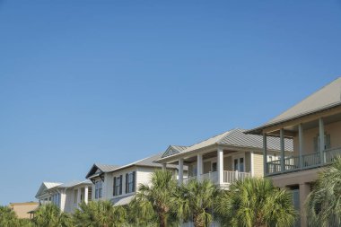 Florida, Destin 'de mavi gökyüzüne karşı evlerin önündeki palmiye ağaçları. Açık mavi arka planda balkonları olan evler..