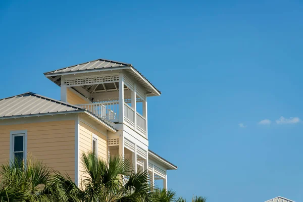 Views of a house with roof deck and palm trees against the clear sky background in Destin, Florida. View of a house with white trims and light yellow wood lap siding.