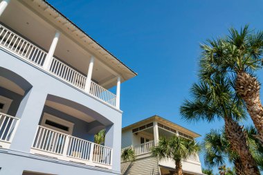 Aralarında palmiye ağaçları olan iki evin alçak açılı görüntüsü. Destin, Florida. Evin dışında solda pastel mavi beyaz korkuluklu ve ahşap kaplamalı bir ev var..