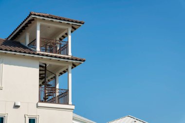 Destin, Florida 'da beyaz duvarı ve kahverengi çatı kiremitleri olan bir binanın yan görüntüsü. Evin dış tarafında iki balkon ve spiral merdiven var..