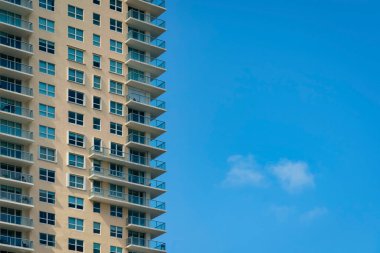 Dış yüzeyinde bej duvar ve balkonlarında cam korkuluklar olan bir apartman dairesi. Miami, Florida. Soldaki çok katlı, sağdaki mavi gökyüzü ise çok katlı modern bir yerleşim yeri..