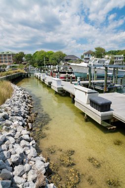 Destin, Florida. Kutular ve teknelerle balıkçı teknesi iskelesi. Suyun yanında solda kayalar ve arkada binalar ve ağaçlar var..