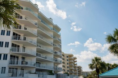 Destin, Florida- Palmiye ağaçları olan apartman daireleri. Gökyüzü zeminine karşı balkonlu apartman manzarası.