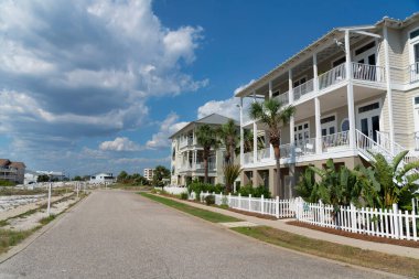 Destin, Florida- üç katlı teraslı evlerin önünde beton yol var. Solda bir yol ve sağda çitli evler var. Önünde tropik bitkiler ve ağaçlar var..