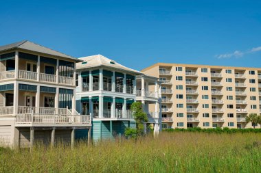 Destin, Florida- Balkonlu ve güverteli üç katlı evler. Konut binalarının önünde uzun otlaklar var..