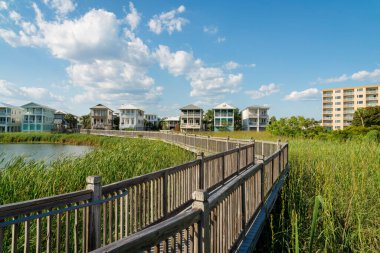 Destin, Florida- Gölün üzerinde tahta tırabzanlar ve uzun çimen bitkileri olan patika. Apartman manzaralı tahta kaldırım ve üç katlı gökyüzü manzaralı evler..