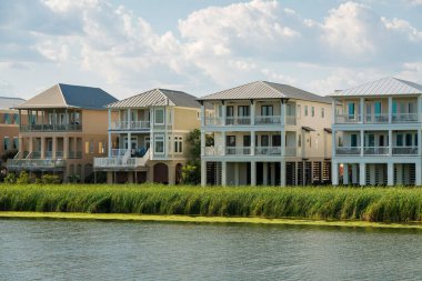 Destin, Florida- Üç katlı evler, güverteler ve göl kıyısında. Cephede bir göl var. Evlerin yanında uzun otlar var..