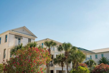 Destin, Florida. Üç katlı evlerin önünde tropikal ve çiçek açan bitkiler. Açık gökyüzüne karşı balkonları olan konut binalarının alçak açılı görüntüsü.