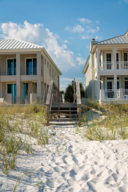 Destin, Florida- Sahildeki evlerin önündeki kum tepelerinin üzerinde tahta bir yaya köprüsünün merdivenleri. Arka planda terasları olan iki sahil evi arasında köprü var..