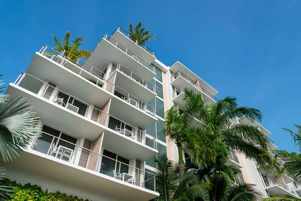 Apartment building with balconies and palm trees on the roof under the blue sky at Miami, Florida. Low angle view of a building with coffee tables at the balconies.