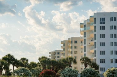 Destin, Florida 'daki dairelerin önünde budanmış begonviller ve palmiye ağaçları. Bulutlu arka planda balkonları olan daireler..