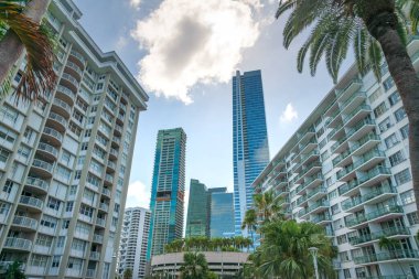 Miami, Florida gökyüzündeki bulutların altında lüks meskenler. Her iki tarafta iki tane orta katlı bina ve ortada da yüksek katlı binalar var..