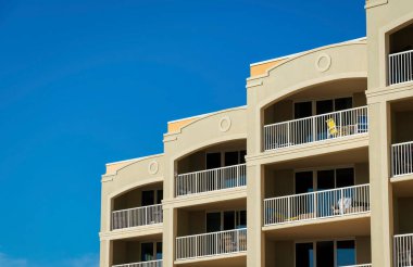 Destin, Florida 'da balkonları olan bir bina. Boyanmış bej duvarlı ve açık mavi arkaplanı olan bir binada şezlonglu balkon manzarası..