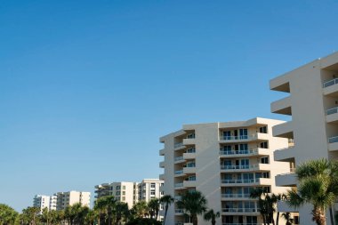 Destin, Florida 'daki modern, orta büyüklükteki konut binaları. Binaların önünde mavi gökyüzünün altında cam balkon korkulukları olan palmiye ağaçları var..