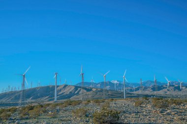 Yel değirmenleri yenilenebilir enerji jeneratörü mavi gökyüzü arka planına karşı. Bir dağ manzarasında alternatif bir yeşil elektrik kaynağı olarak rüzgar pompaları.