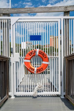 Destin, Florida- Orange cankurtaran şamandırası ve sadece kapalı beyaz bir kapıda asılı duruyor. Tuş takımı kilidi ve arka plandaki rıhtım manzaralı kapıda bir can simidi..