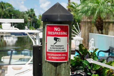 Miami, Florida 'da kapaklı ahşap iskeleye izinsiz giriş yok. İzinsiz girenler için teknelere karşı güvenlik kamerası sembolü ve arkada ahşap duvar olan bir uyarı levhası yakın plan..
