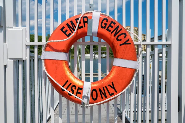 Destin, Florida- Lifebuoy ring with Emergency Use Only lettering. Hanging lifebuoy on a white gate railings against the view of water at the background.
