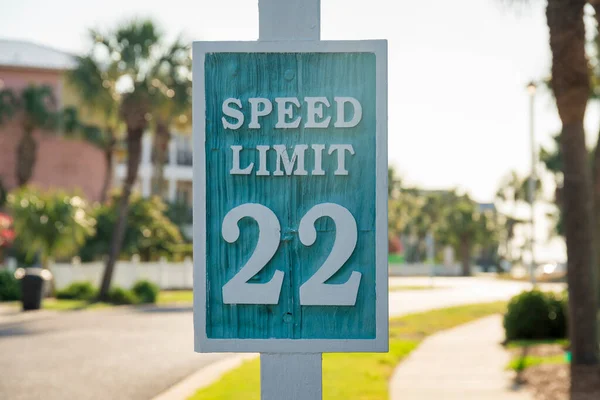 Destin, Florida- Carved road sign with Speed Limit 22. Signage close-up against the view of the sidewalk on the right and grass in between the road on the left.