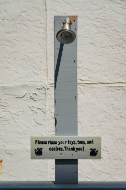 Destin, Florida- Lütfen oyuncaklarınızı, ayak parmaklarınızı ve soğutucularınızı durulama alanında yıkayın. Su musluğunun altındaki gri tahta levha ile durulama alanı.