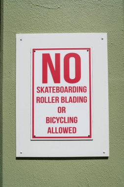 Destin, Florida. Kaykay, patenle kayma ya da bisiklet sürmeye izin verilmeyen bir tabelanın yakın çekimi. Boyanmış zeytin yeşili bir duvara kırmızı harflerle yazılmış beyaz tabela..