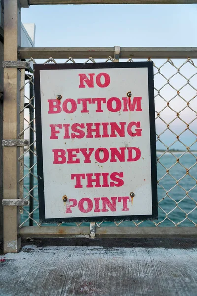 stock image Destin, Florida- No Bottom Fishing Beyond This Point signage on a chain link barrier at the pier. Close-up sign on a barrier with a view of the ocean at the background.