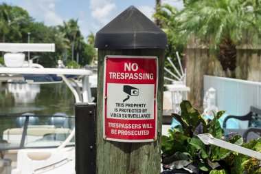 Miami, Florida 'da kapaklı ahşap iskeleye izinsiz giriş yok. İzinsiz girenler için teknelere karşı güvenlik kamerası sembolü ve arkada ahşap duvar olan bir uyarı levhası yakın plan..