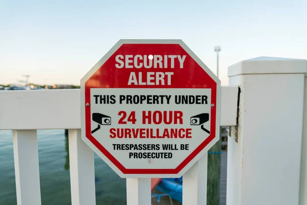 Security Alert This Property Under 24 Hour Surveillance sign on a railings at Destin, Florida. Close-up of a signage of a private property near the sea.