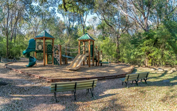 Austin, Texas- Community park with bench seats near the playground. There are two seats at the front against the playground with green trees at the background.