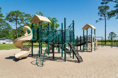 Destin, Florida. Engelli ve ağaçların olduğu bir oyun parkı. Açık mavi gökyüzü arkaplanına karşı bir kumdaki oyun alanı.