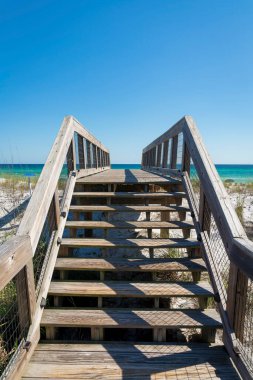 Destin, FL 'de, okyanus manzaralı beyaz kum tepelerinin üzerinde tahta merdivenler. Kum tepelerinin üzerinde sahil yürüyüşü ve okyanus ve gökyüzü manzarası.