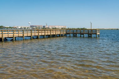 Destin, Florida 'daki binaların manzarasına ve mavi gökyüzüne karşı ahşap iskele. Sahilden lamba direkleriyle iskele manzarası.