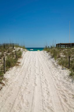 Destin, Florida plajına doğru ilerleyen otlarla dolu beyaz bir off-road. Açık gökyüzü arkaplan üzerinde tekerlek izleri ile ortadaki yol.
