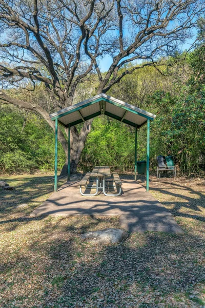 Austin, Texas- Community park with picnic table under a roof. Covered dining area against the view of green trees at the forest background.