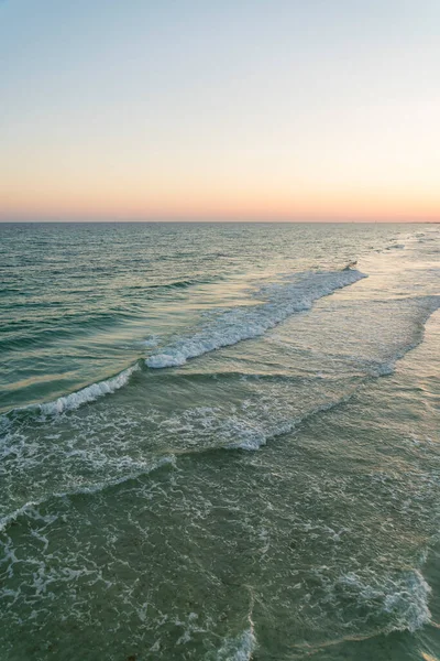 Calm ocean waves against the sunset skyline horizon in Destin, Florida. Vertical shot of a seascape sunset on a clear sky above the ocean water.