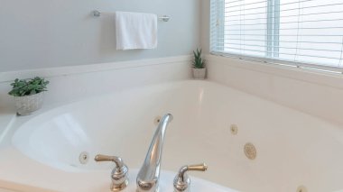 Panorama Köşesi küveti, içinde saksı bitkileri ve geniş bir musluk var. Pencerenin yanında jaluzili bir banyo..