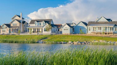 Panorama White puffy clouds Panoramic view of blue waters of Oquirrh Lake at Daybreak in South Jordan, California. Residential area with lake waterfront with tall grasses at the front.
