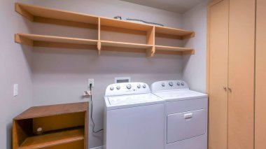 Panorama Çamaşırhanesinin içinde dolap, ahşap raflar ve raflar var. Sağda, dolabın yanında, rafların altındaki rafın yanında çamaşır makineleri var..