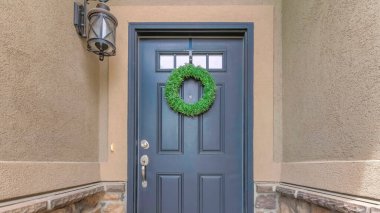 Büyük paspası, cam paneli ve çelengi olan Panorama Gri ön kapısı. Duvarın ortasında beton ve taş kaplamalı ev girişi..