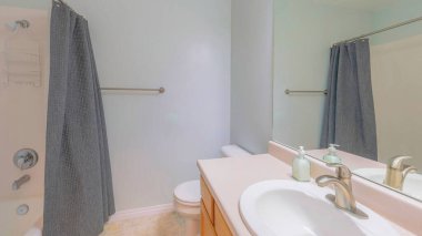 Panorama banyosu. İçi kızarık mavi ve döşemeleri seramik. Duş başlığı asılı bir küvet duşu var. Çanta taşıyıcısı ve gri duş perdesi lavabonun yanında, aynalı..