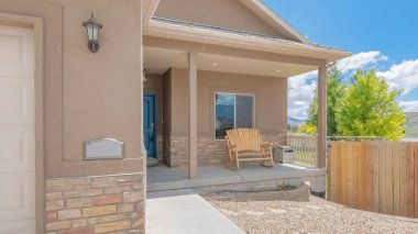 Panorama Beyaz Kabarık Bulutları ön bahçesinde ahşap çitli ve çakıllı ev dışında. Beyaz bölmeli kapısı olan bir garaj ve solunda mavi kapısı olan ahşap bir bank var..