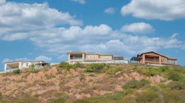 Panorama Beyaz kabarık bulutları alçak açılı tepe manzaralı Double Peak Park, San Marcos, California 'da evleri var. Tepenin kayalık yamacında çalılar ve çalılar var. Açık gökyüzüne karşı yerleşim alanları var..