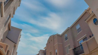 Panorama Whispy beyaz bulutları San Marcos, California 'daki apartmanların alçak açılı görüntüsü. Dış görünüşü balkonlu ve açık mavi gökyüzü arkaplanlı kompleks apartmanlar..