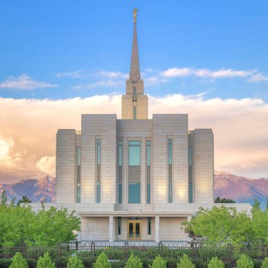 Gün batımında Kare Kabarık Bulutlar Utah 'ta dağlara ve günbatımına karşı çitli bir LDS kilisesi cephesi. Çan kulesi olan kilise binası, camlı çift kapılı altın kapılı ve mermer kaplamalı..