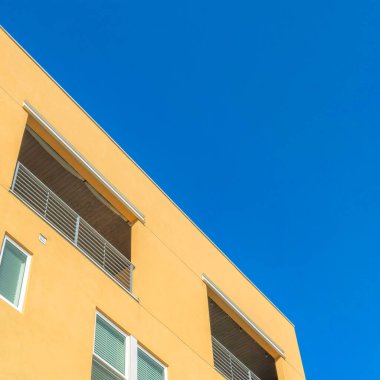 Güney Ürdün, Utah 'ta, Daybreak' teki sarı bir binanın alçak açılı görüntüsü. Balkonunda metal parmaklıkları olan, temiz gökyüzü arka planına karşı inşa edilmiş bir bina..