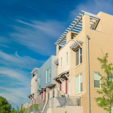 Kare Fısıldayan Beyaz Bulutlar, Utah, Güney Ürdün 'deki Daybreak' te merdivenlere merdiven dayamış konut binaları oluşturdu. Binaların önünde solda beton bir kaldırım ve sağda çimenler var..