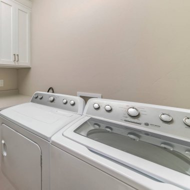 Üst dolapları ve tezgahı olan bir çamaşırhanenin içi. Tezgahın sağında, beyaz ahşap kapılı dolapların altında iki çamaşırhane var..