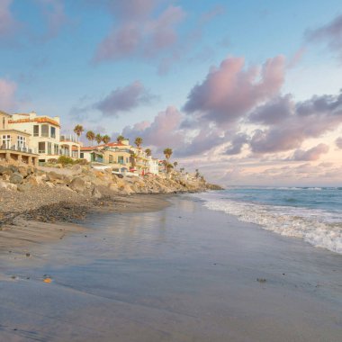 Gün batımında Kare Kabarık Bulutlar Oceanside, California 'da sahil kenarlı devasa binalar. Kumlu kumlu bir sahil manzarası var. Kaya deniz kenarında çakıl taşları var..